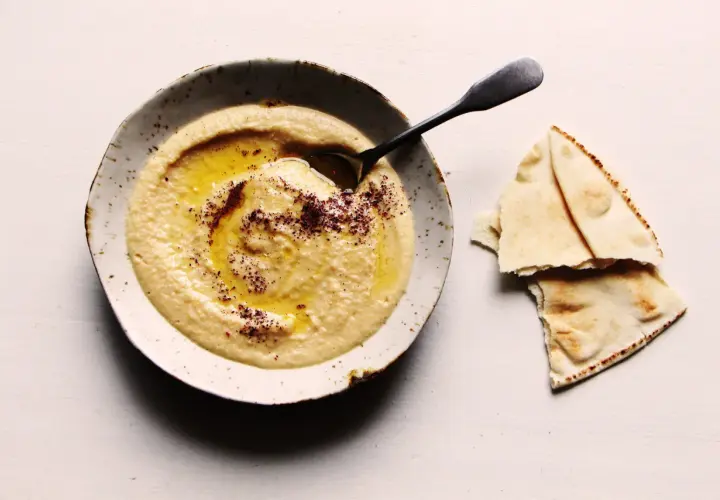 Un bol de houmous onctueux, arrosé d'huile d'olive et saupoudré d'épices, prêt à être dégusté avec du pain pita. Une recette houmous simple et savoureuse.