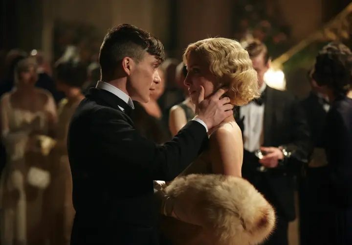 Tommy Shelby czule dotyka policzka Grace, jednej z kluczowych kobiet w świecie Peaky Blinders. W tle widać innych gości balu.