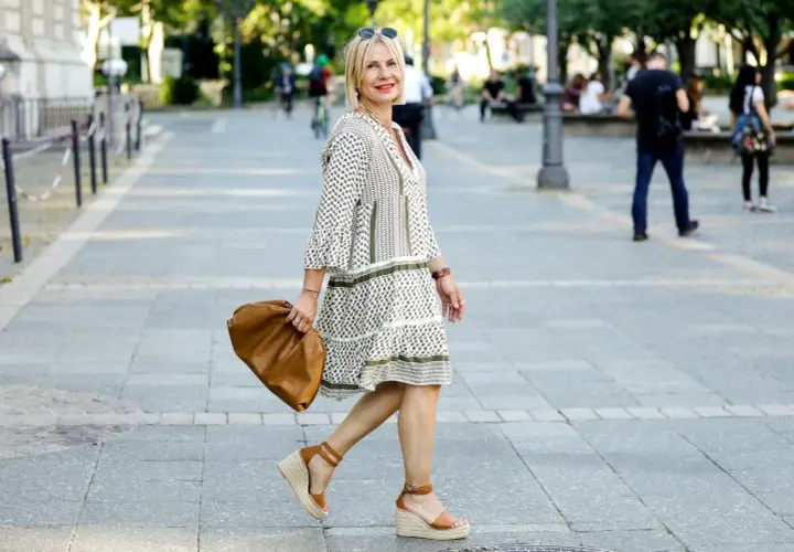Elegancka kobieta w sukience i espadrylach damskich stylizacjach, z brązową torebką, spaceruje po mieście.