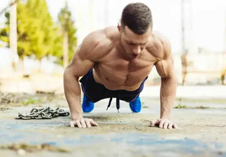 Mięśniowy mężczyzna wykonuje pompki na biceps, z łańcuchem obok.