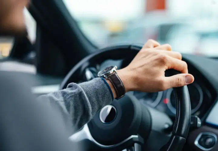 Mano en el volante, reloj de pulsera, tablero de coche. El conductor nota un fallo en la dirección asistida.