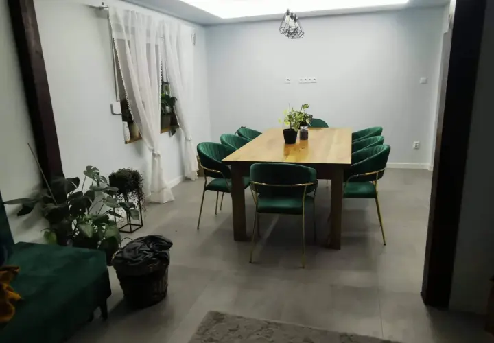 Elegancki salon w stylu glamour z zielonymi aksamitnymi krzesłami i drewnianym stołem.