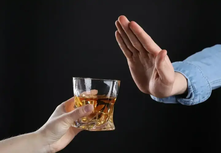 Ręka odrzuca szklankę z bursztynowym płynem. Czy dzień przed wizytą u dentysty można pić alkohol? Lepiej nie ryzykować.