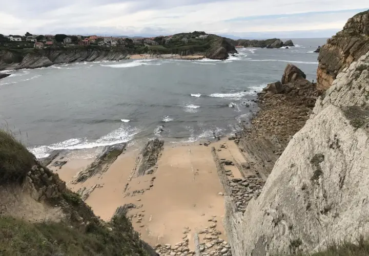 Vista panorámica de la playa San Juan de la Canal, con formaciones rocosas y casas en la costa.