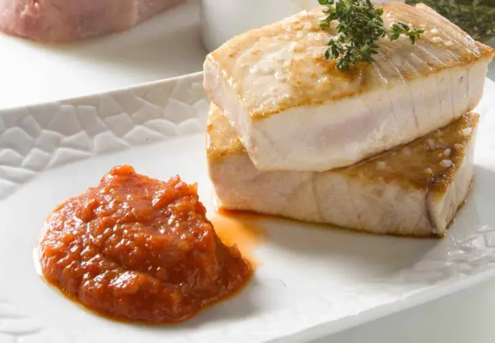 Dos jugosos medallones de atún a la plancha, con sal gruesa y romero, acompañados de una cucharada de salsa de tomate casera.