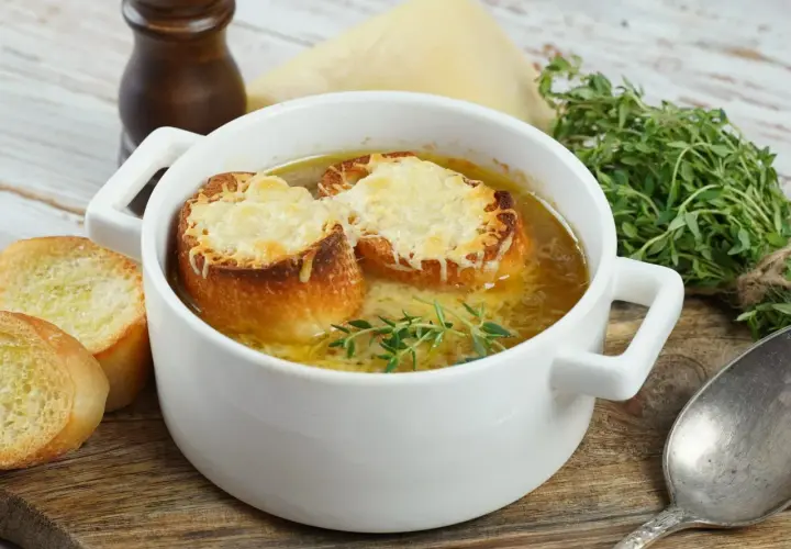 Aksamitna zupa cebulowa przepis, podana w białej miseczce z grzankami zapieczonymi z serem i gałązką tymianku.