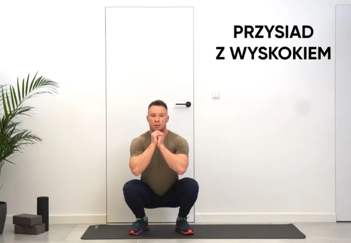 Mężczyzna w pozycji do przysiadów z wyskokiem, gotowy do ćwiczeń.