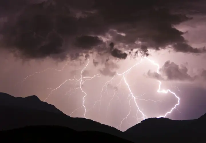 Gewitter in den Bergen: Blitze zucken durch dunkle Wolken über silhouettierten Gipfeln.