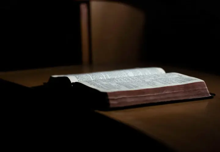 Otwarta Biblia na drewnianym stole, światło pada na strony. Słowa mądrości trwają, dopóki ziemia kręci się.