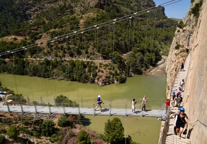 Visitantes caminan por la pasarela del Caminito del Rey, una impresionante ruta del rey entre acantilados y un río verde.