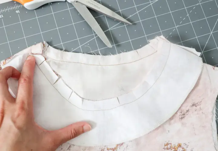 A hand guides the inner facing of a garment, showing the clipped seam allowance for a smooth neckline finish.