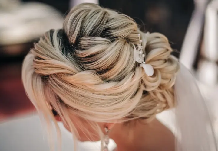 Elegancki, luźny warkocz ślubny z delikatną ozdobą z kryształków i piórka.