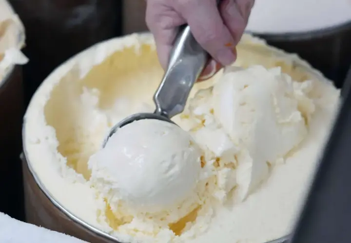 Eine Hand schöpft cremiges Vanilleeis aus einem großen Behälter. Die Eismaschine hat ganze Arbeit geleistet!