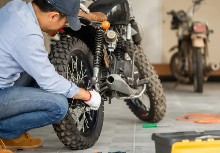 Mecánico revisa moto para su homologación. Herramientas y otra moto en el fondo.