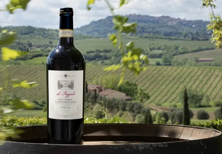 Bottiglia di Vino Nobile di Montepulciano su una botte, con vigneti e colline toscane sullo sfondo. Un invito a una visita cantina Montepulciano.