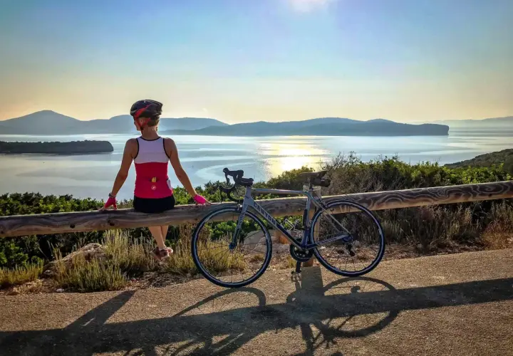 Ciclista descansa tras un tour en bicicleta en Cerdeña, disfrutando de la vista al mar al atardecer.