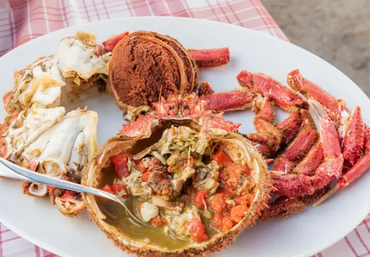 Centollo marisco preparado en una fuente blanca, con su coral y patas rojas. Una cuchara sirve el interior jugoso.