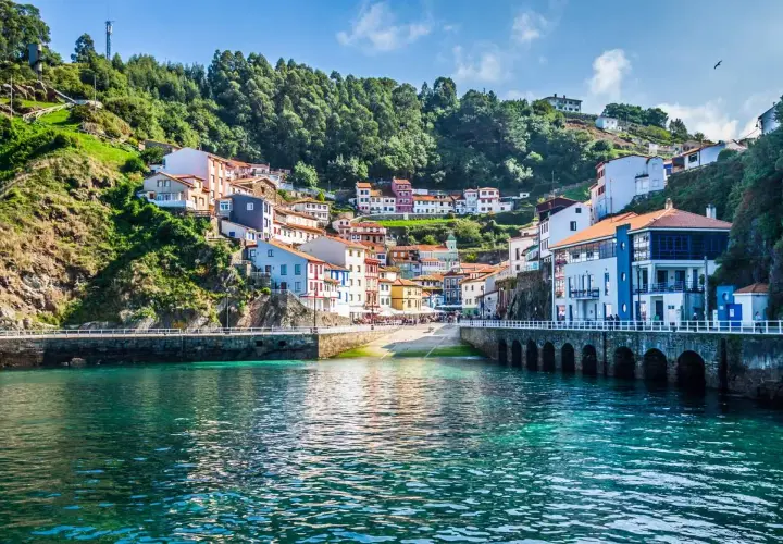 Un pueblo costero con casas coloridas se aferra a una colina verde. Un lugar perfecto para una escapada de pueblos con encanto.