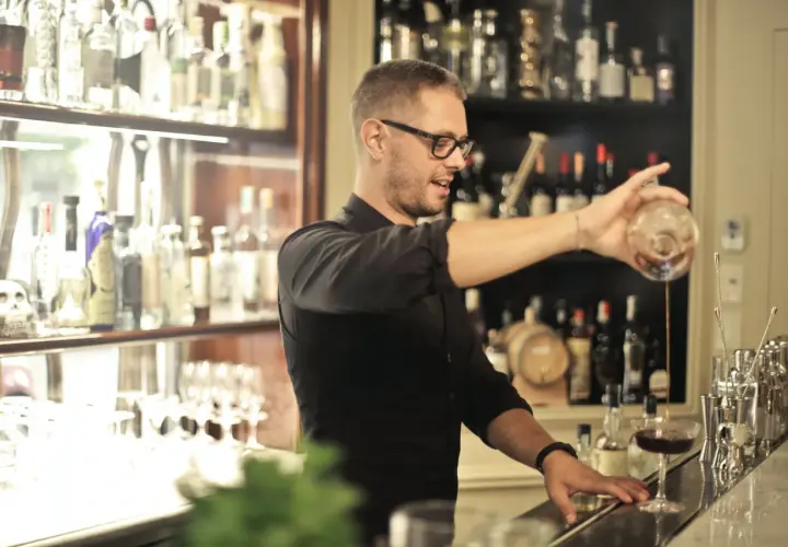 Barman w okularach nalewa drinka. Zastanawiasz się, ile się zarabia jako barman? To zależy od lokalu i doświadczenia.