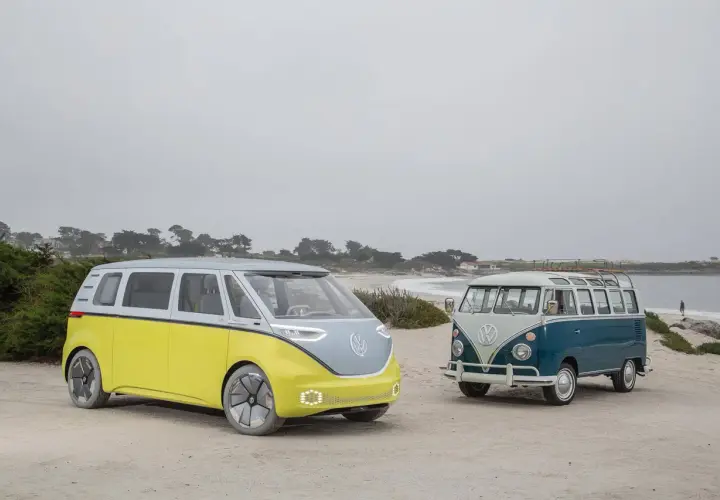 Deux combi VW, un moderne jaune et gris, l'autre vintage bleu et blanc, sur une plage brumeuse.