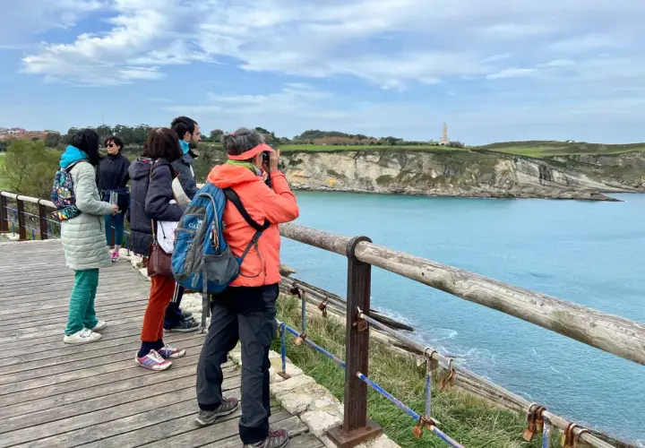 Disfrutando de las rutas por Santander, un grupo de amigos admira el faro y la costa desde un mirador de madera.