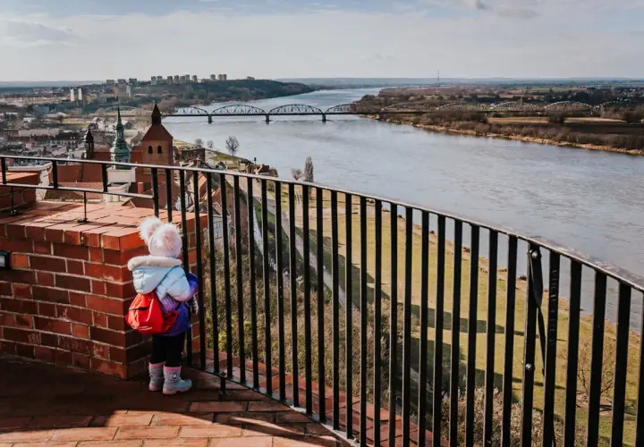 Dziecko z plecaczkiem podziwia panoramę Grudziądza i Wisły. Widok na mosty i miasto to jedne z głównych atrakcji.