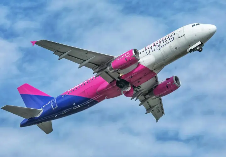 Samolot Wizz Air z różowo-niebieskim ogonem wznosi się na tle błękitnego nieba.