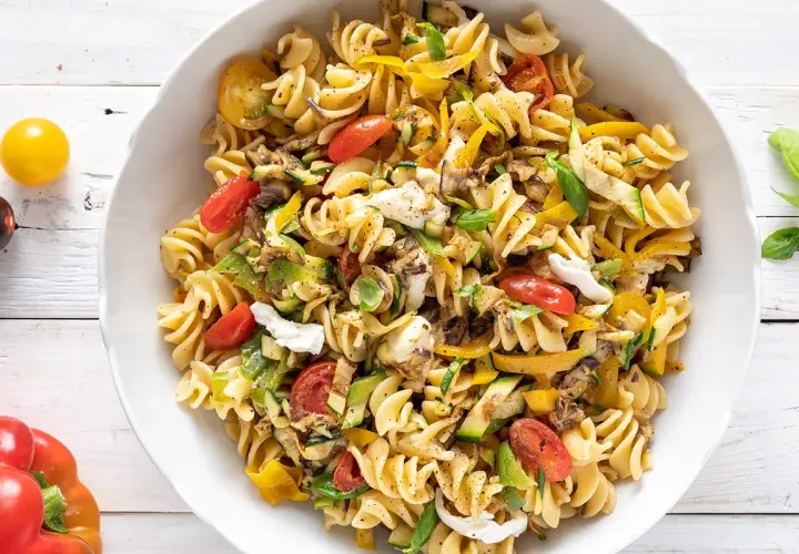 Un piatto invitante di pasta fredda saporita con fusilli, pomodorini, zucchine, peperoni gialli e mozzarella.