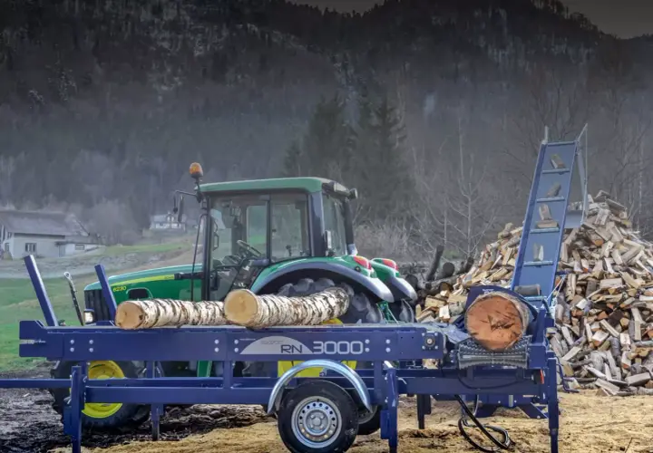 Ein Taifun Holzspalter mit Traktor im Hintergrund, bereit, einen großen Holzstapel zu verarbeiten.