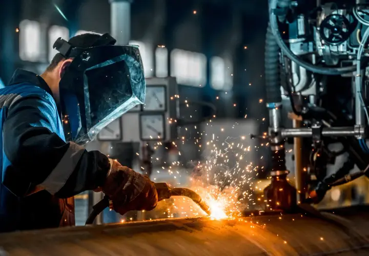 Spawacz w masce ochronnej używa elektrod do aluminium, tworząc iskry podczas pracy przy metalowej konstrukcji.