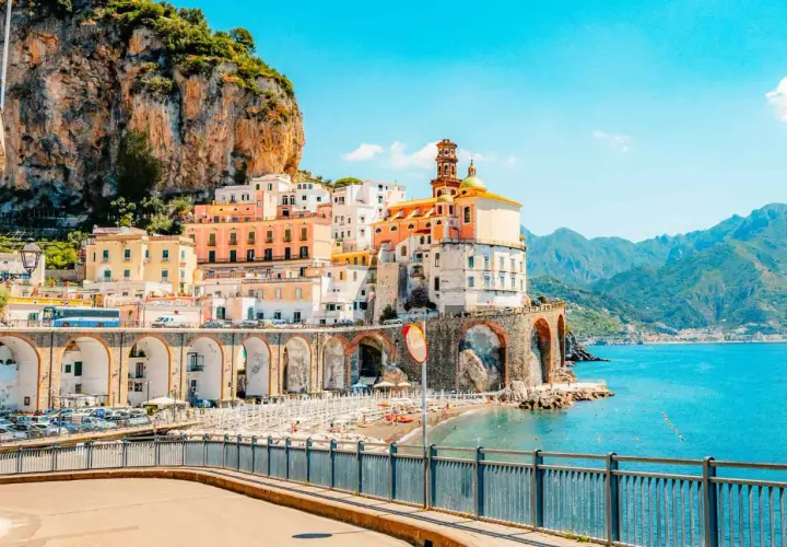 Colorful buildings cling to a cliffside overlooking a beach and the turquoise sea, a quintessential view of Amalfi Coast cities.