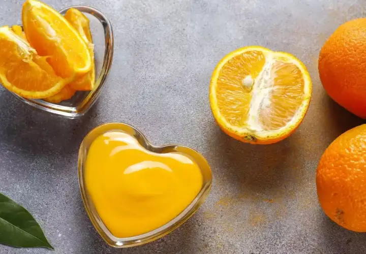 Arance fresche, spicchi e succo in ciotole a forma di cuore. Scopri quale alimento contiene più vitamina C per un cuore sano!