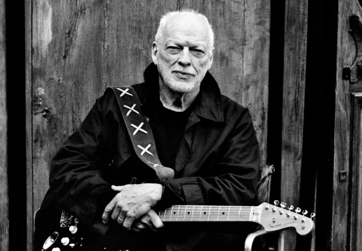 David Gilmour z najdroższą gitarą na świecie, oparty o drewniane drzwi.