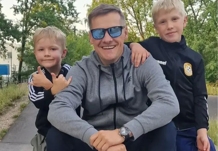 Marcin Mroczek z uśmiechem i dwoma synami, którzy go obejmują. Radosny dzień ojca i dzieci.