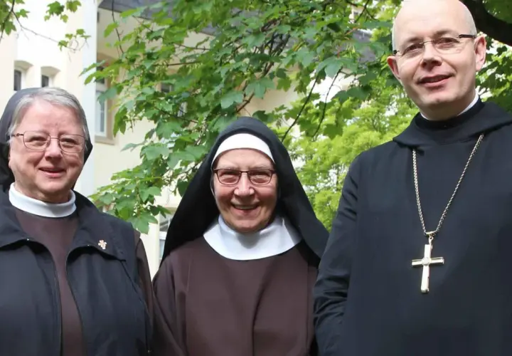 Drei Geistliche, zwei Nonnen und ein Priester, stehen lächelnd vor einem Gebäude. Sie repräsentieren katholische Orden.