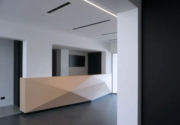Moderno bancone reception in cartongesso con pannelli geometrici in legno chiaro.