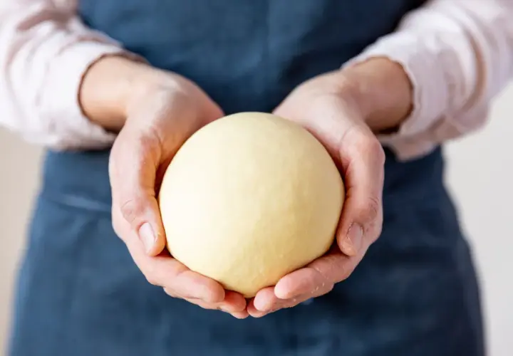 Hände halten einen glatten, gelben Ball aus nudelteig ohne ei.