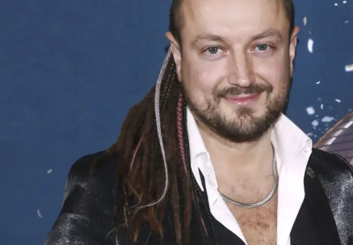 Aleksander Milwiw-Baron, znany z charakterystycznych dredów, z uśmiechem na twarzy. Jego pochodzenie jest często tematem dyskusji.