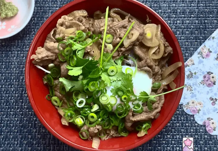A delicious wagyu donburi with thinly sliced beef, onions, and a perfectly poached egg, garnished with fresh scallions and cilantro.