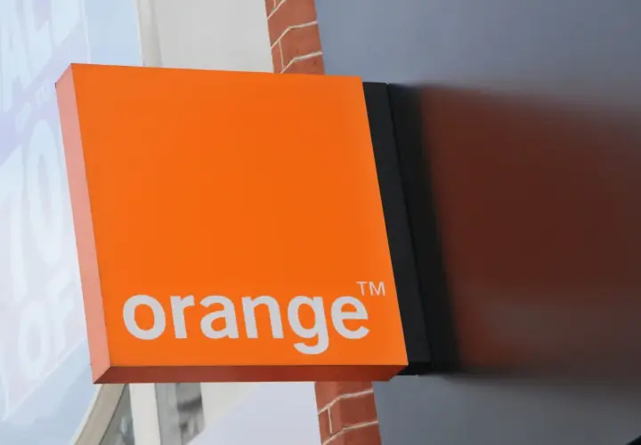 Pomarańczowy szyld Orange z napisem "orange" i symbolem ™. Obok widać fragment okna z napisem "SALE UP TO 70% OFF", sugerujący promocje i kody rabatowe.