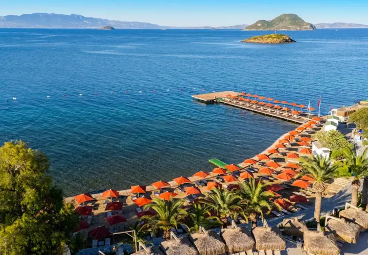 Piękna plaża z rzędem pomarańczowych parasoli i leżaków, drewniany pomost, palmy i turkusowe morze. Idealne miejsce na wakacje, zgodnie z kadikale resort opinie.