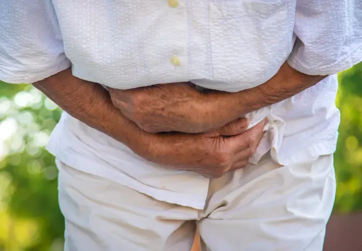 Persona anziana con mani sull'addome, che suggerisce disagio. Potrebbe essere utile sapere cosa prendere per andare in bagno in queste situazioni.