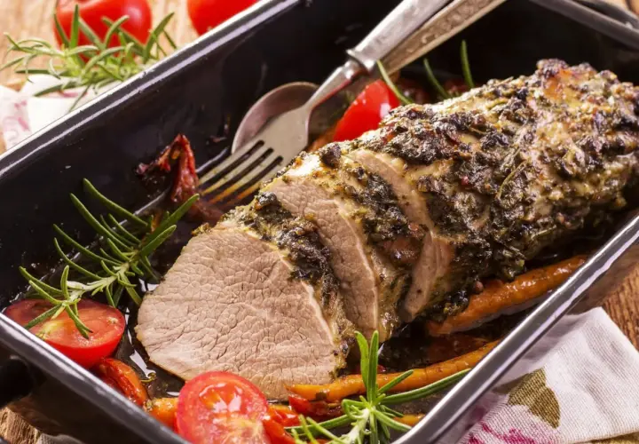 Un délicieux roti de veau aux herbes, servi dans un plat avec des tomates cerises et du romarin.
