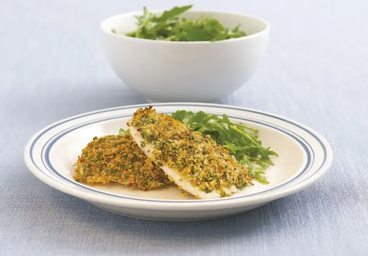Zwei Filets Fisch mit knuspriger Parmesankruste und Rucola auf einem Teller.