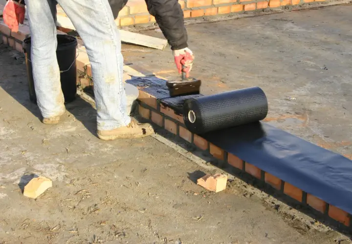 Pracownik nakłada na mur materiały hydroizolacyjne z rolki, zabezpieczając budynek przed wilgocią.