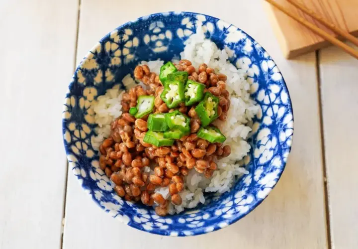 A bowl of natto with rice, topped with sliced okra. This healthy Japanese dish is ready to be enjoyed with chopsticks.