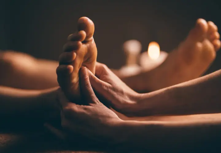 Mains expertes prodiguant un massage plantaire, révélant les bienfaits d'une détente profonde. Bougies tamisées en arrière-plan.