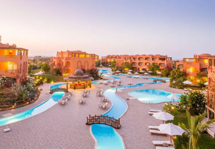 Dream Lagoon & Aqua Park Resort: malowniczy widok na kompleks basenów i budynków w ciepłych barwach, z mostkami i leżakami.