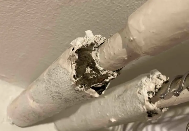 Skadad asbestisolering på rör. Materialet är vitt och smuligt, med synliga fibrer inuti.