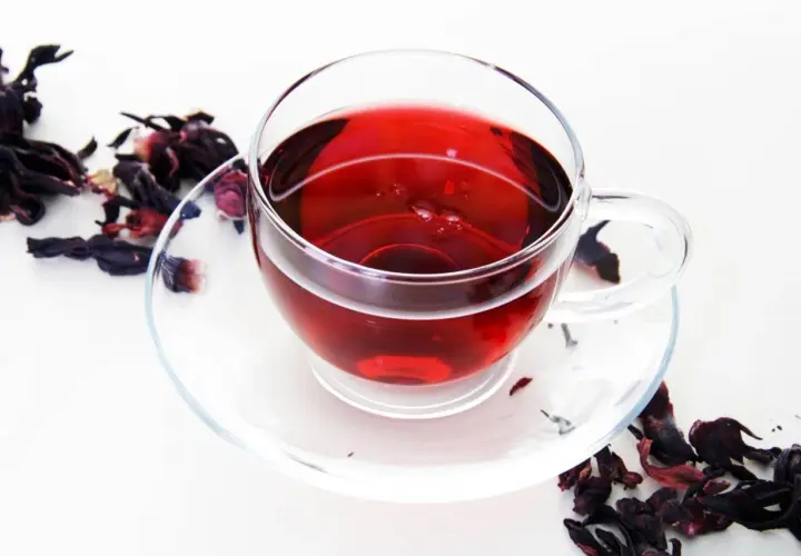 Szklana filiżanka z naparem z hibiskusa, otoczona suszonymi kwiatami. Czerwona herbata właściwości zdrowotne.